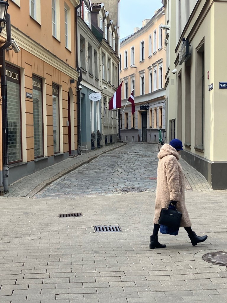 Image of woman walking past Latvian flag. 
