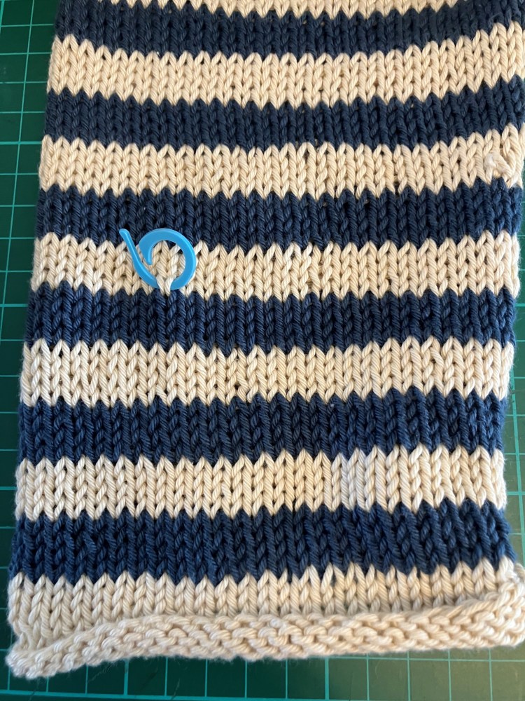 Close-up of a knitted fabric in navy and cream striped pattern with a blue stitch marker secured in place.